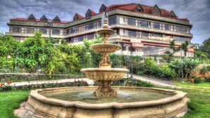 A large, ornate fountain in a garden with a multi-story building in the background. - Ravine Hotel (Mahabaleshwar)