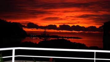 Vista al tramonto da un balcone con ringhiera, su un'area d'acqua e terraferma in lontananza.