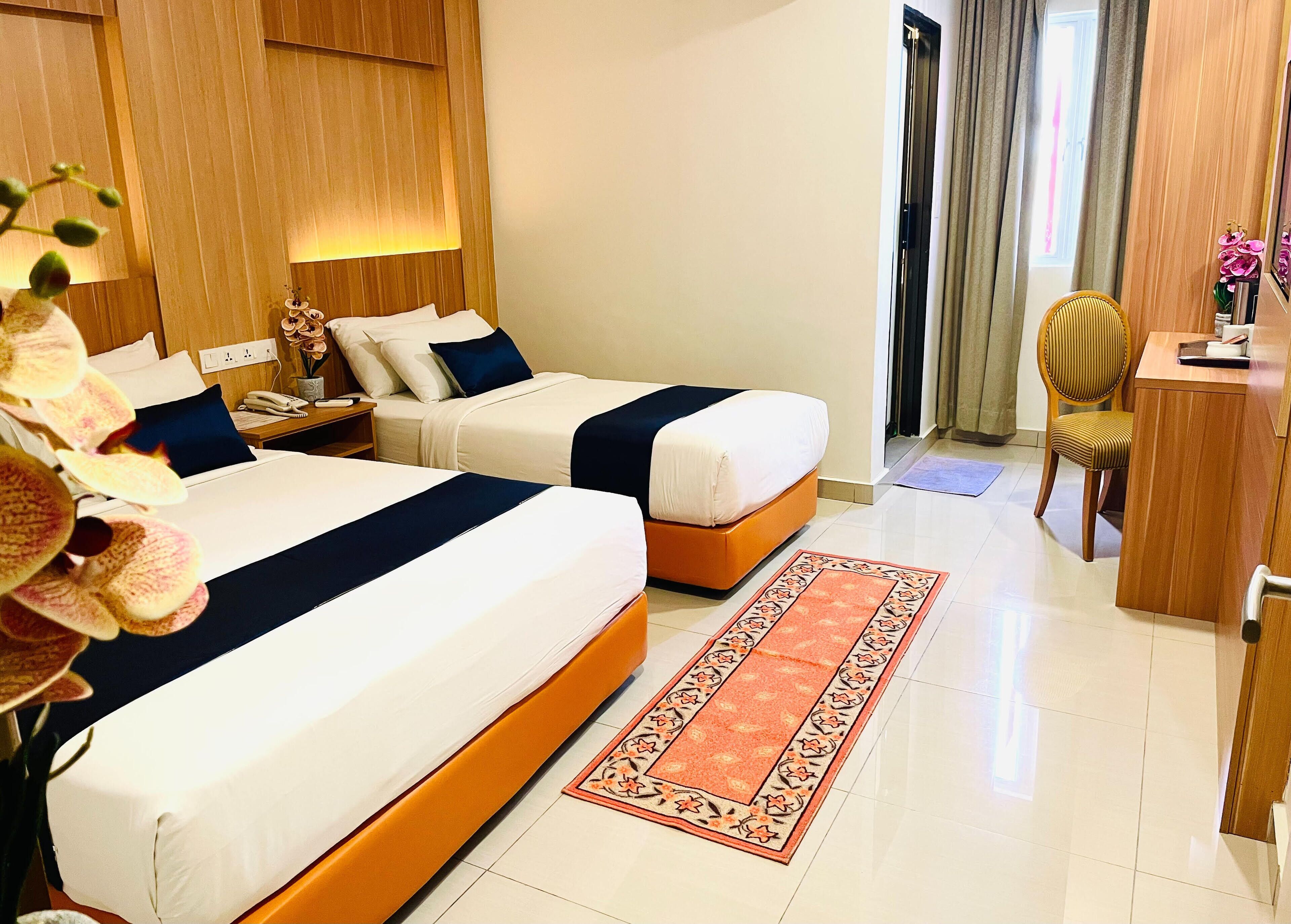 Habitación de hotel con dos camas, un escritorio, una silla y una mesita con un florero.