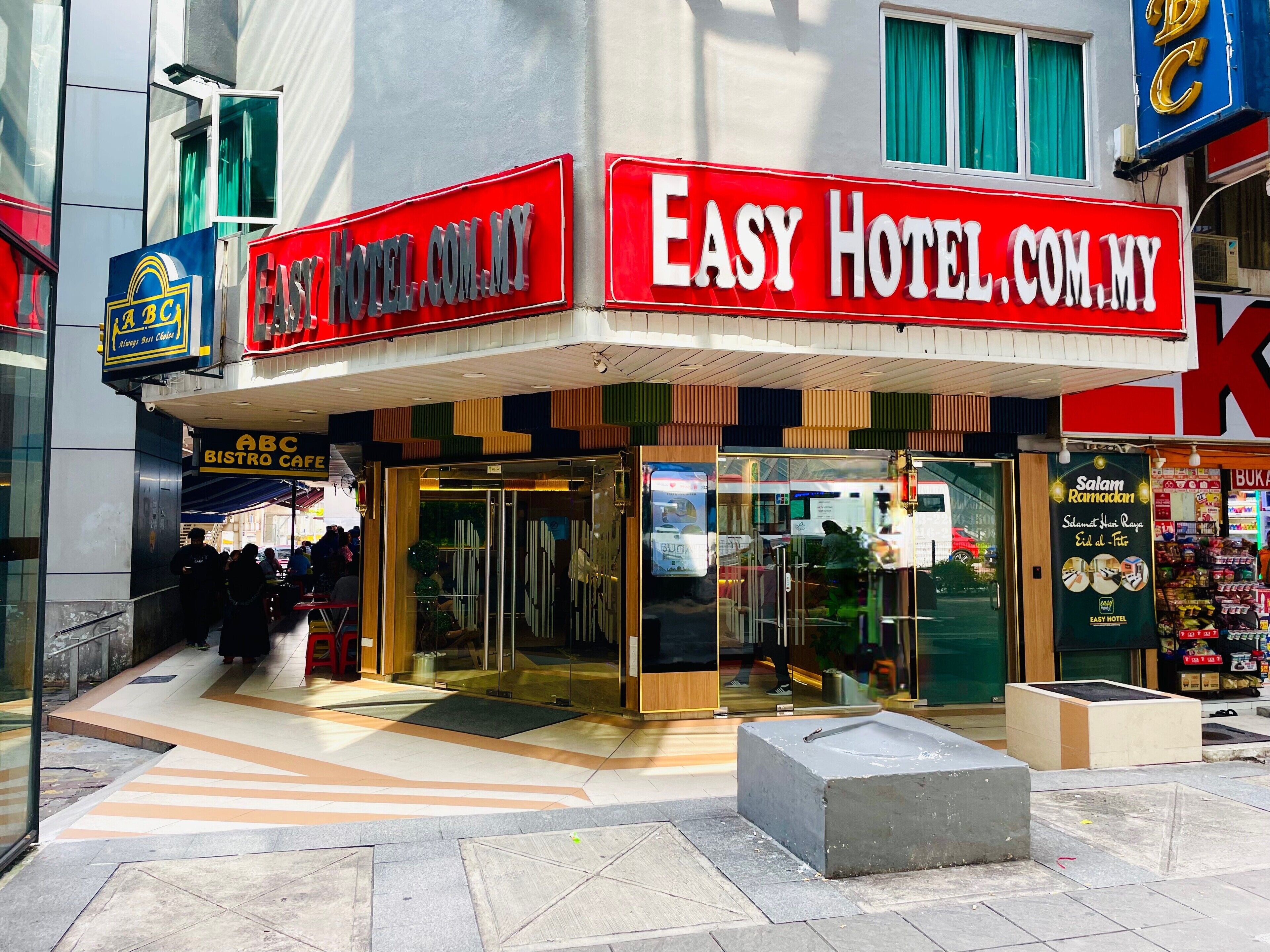 A hotel entrance with a glass facade, a sign for ABC Bistro Cafe, and a prominent Easy Hotel sign.