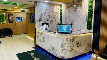 A hotel reception area with a marble counter, a digital display, and a green wall with plants.