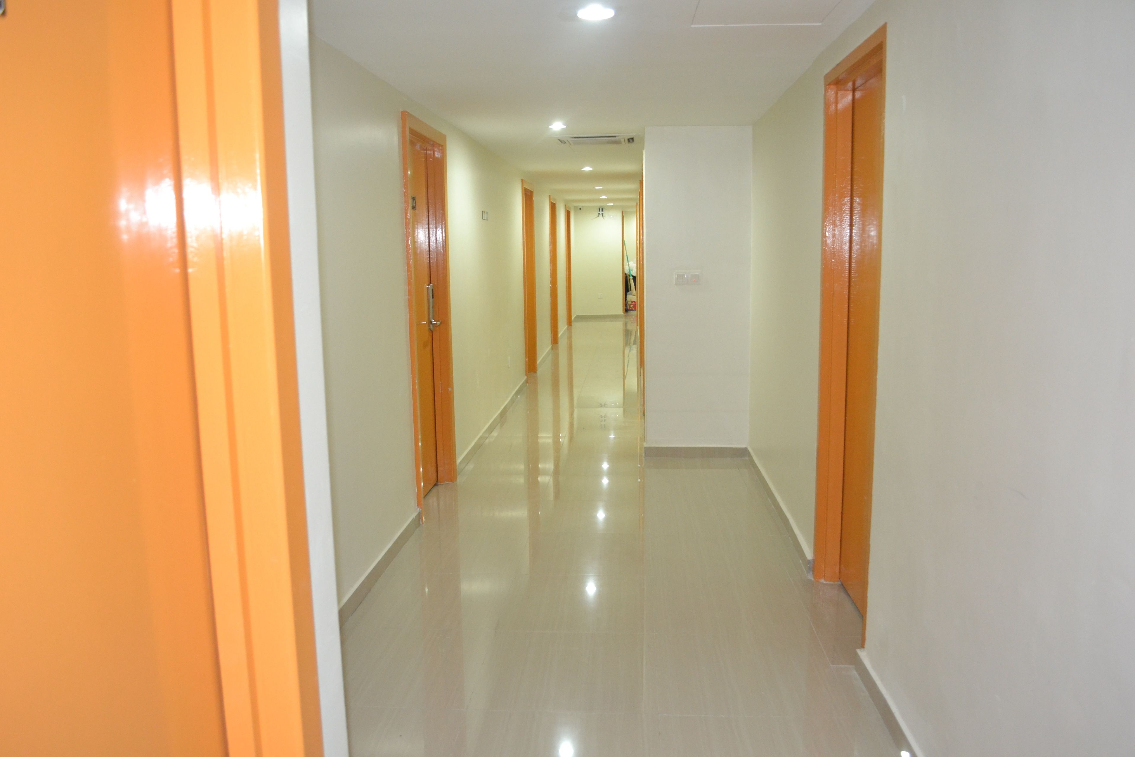 A long, well-lit hallway with orange doors and a shiny floor, leading to a bright room at the end.