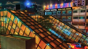 Um hotel bem iluminado com design arquitetônico moderno, apresentando uma fachada de vidro proeminente e um letreiro digital exibindo o nome e o número de contato do hotel.