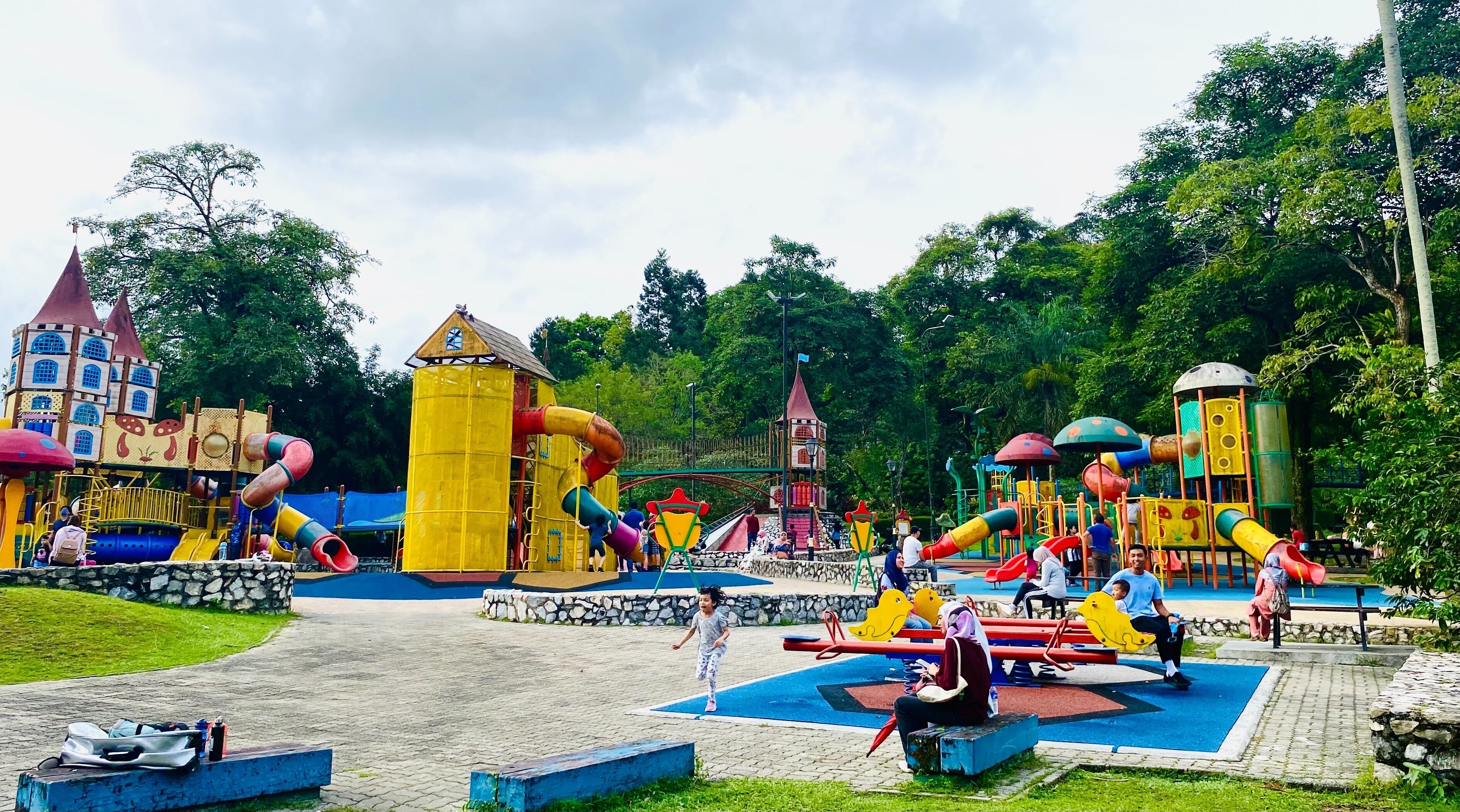 Un parque infantil con diversas estructuras de juego, incluyendo toboganes y zonas de escalada, rodeado de vegetación.