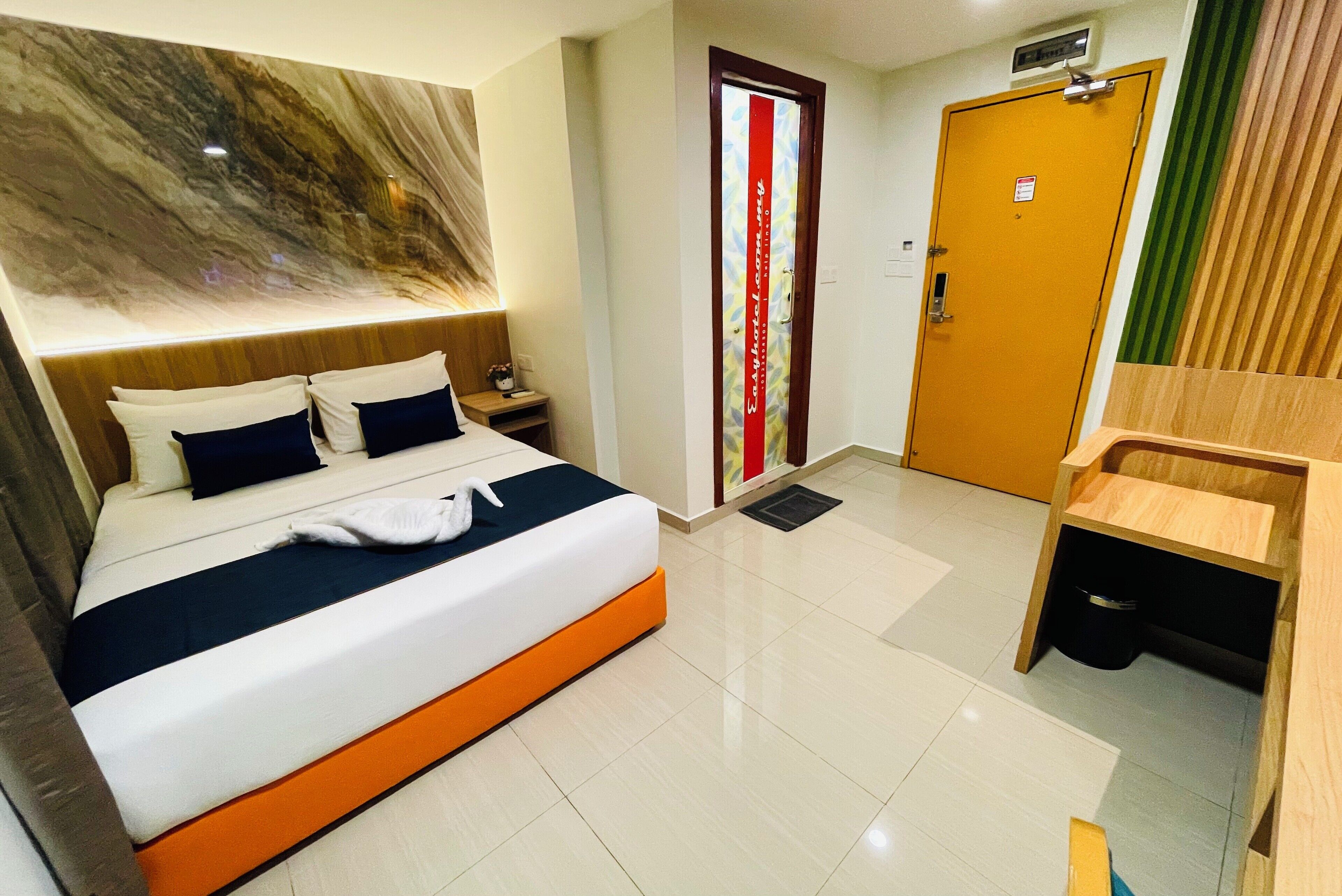 A hotel room with a bed, a nightstand, a wooden bench, a door with a red stripe, and a wall with a marble-like design.