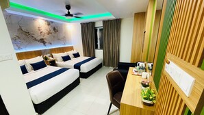 Quarto de hotel com duas camas, uma escrivaninha, uma cadeira, um ventilador de teto e um painel decorativo na parede.