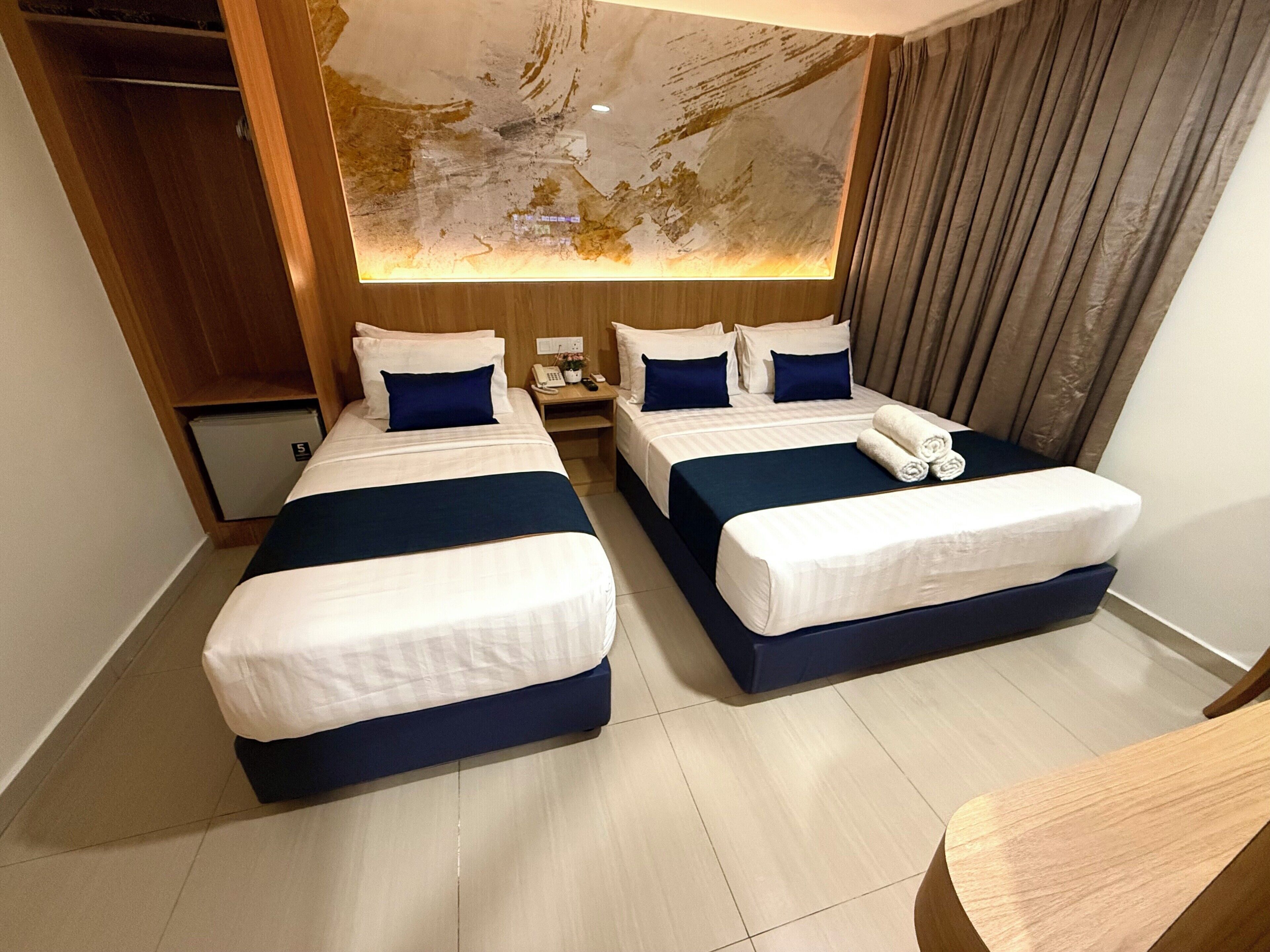 A hotel room with two beds, a small desk, a nightstand, and a large abstract wall art piece.