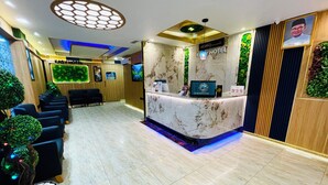 Uma área de recepção de hotel com balcão de mármore, assentos e parede verde.