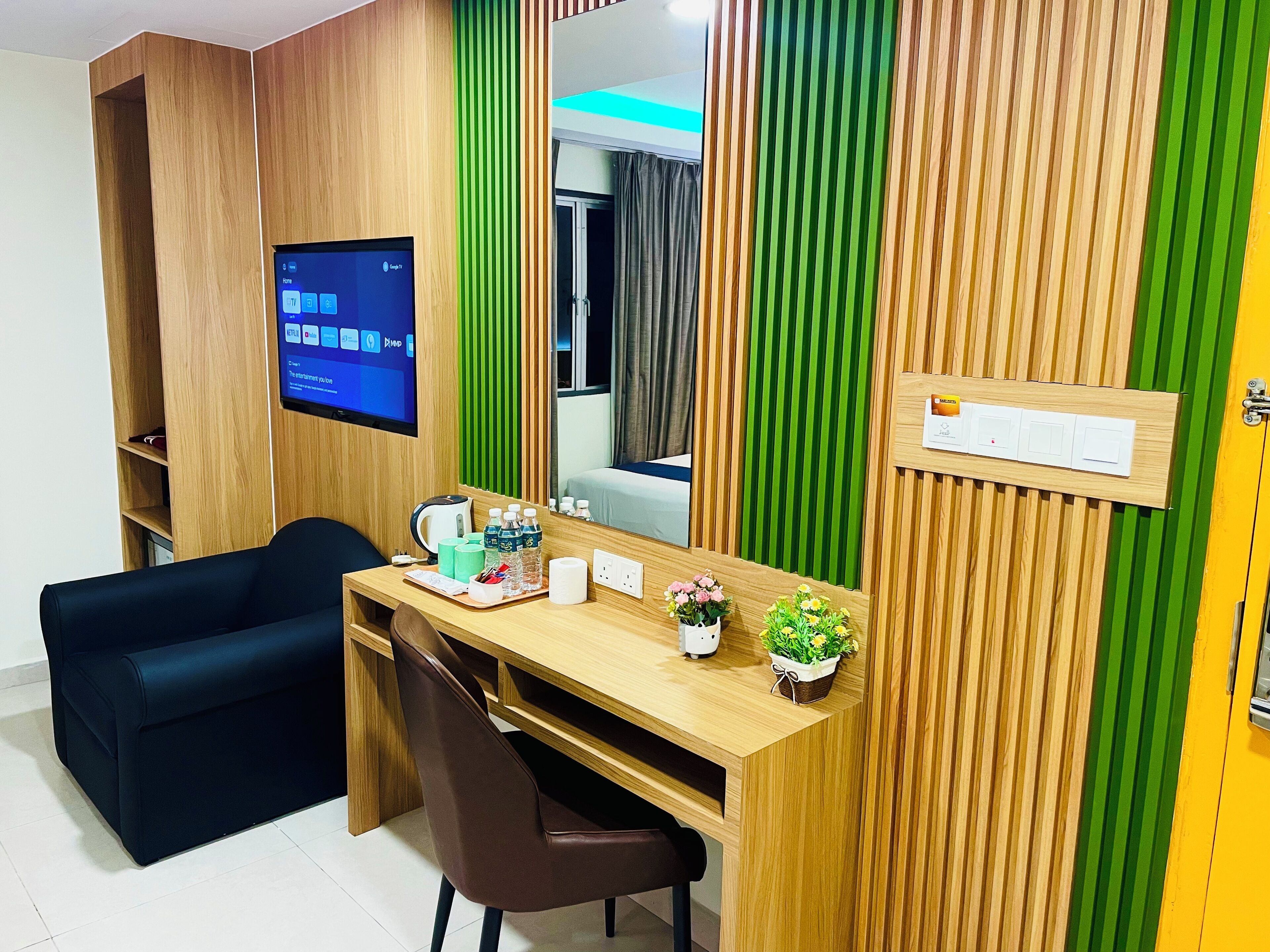 A modern hotel room with a wooden desk, a black sofa, a flat-screen TV, and a mirror.