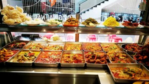 Buffet com diversos pratos, incluindo curry e arroz, dispostos em bandejas de metal.