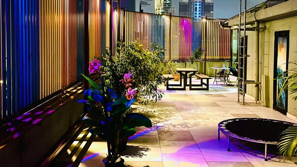 Terraço no telhado com vista para o horizonte urbano, incluindo um arranha-céu imponente. Há plantas em vasos e áreas de estar ao ar livre.