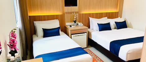 A hotel room with two beds, a desk with a telephone, and a small table with a vase and bottles.