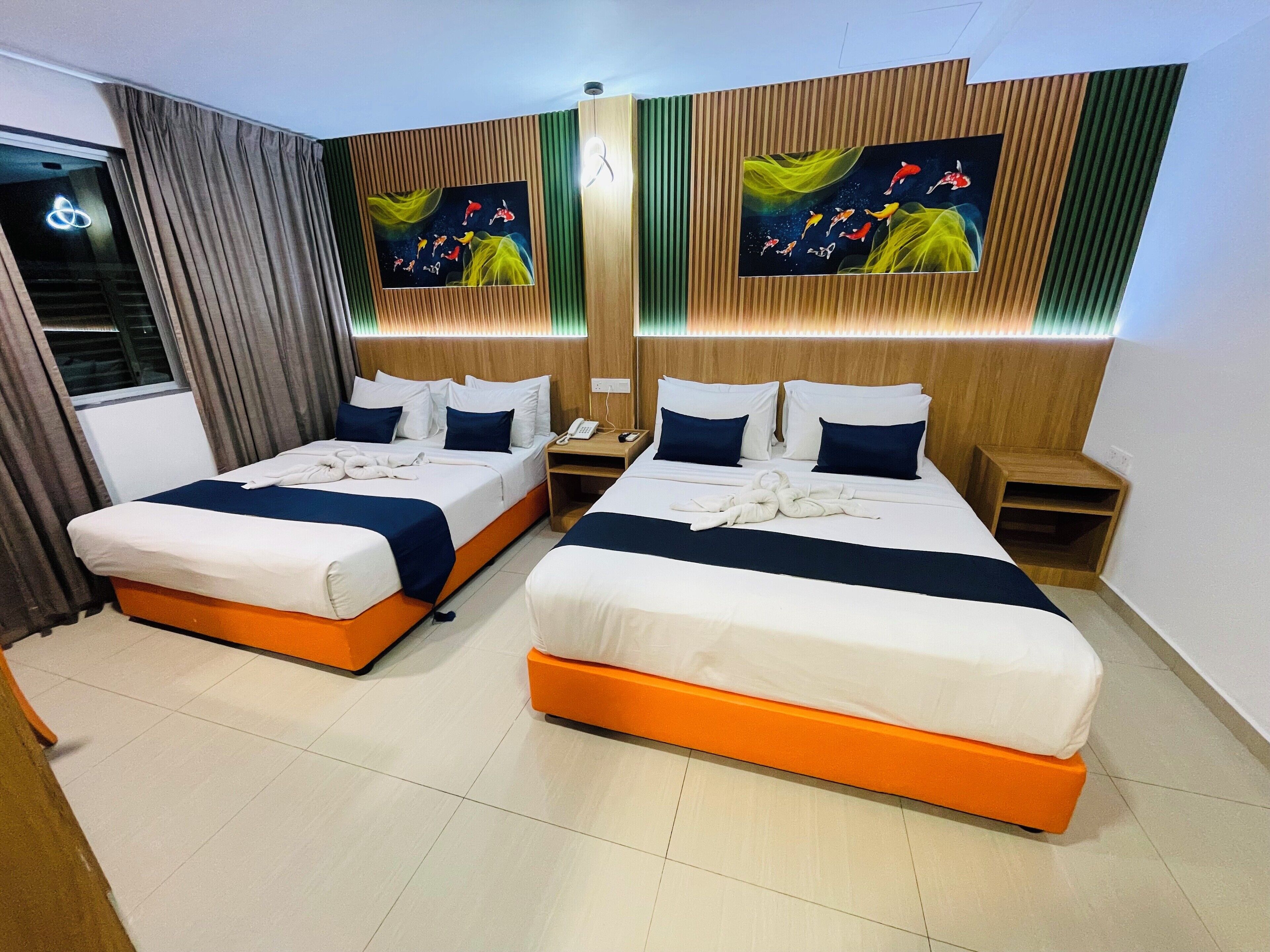 A hotel room with two beds, each with white and blue bedding, and a wooden headboard. There are two paintings on the wall, a nightstand, and a window with curtains.