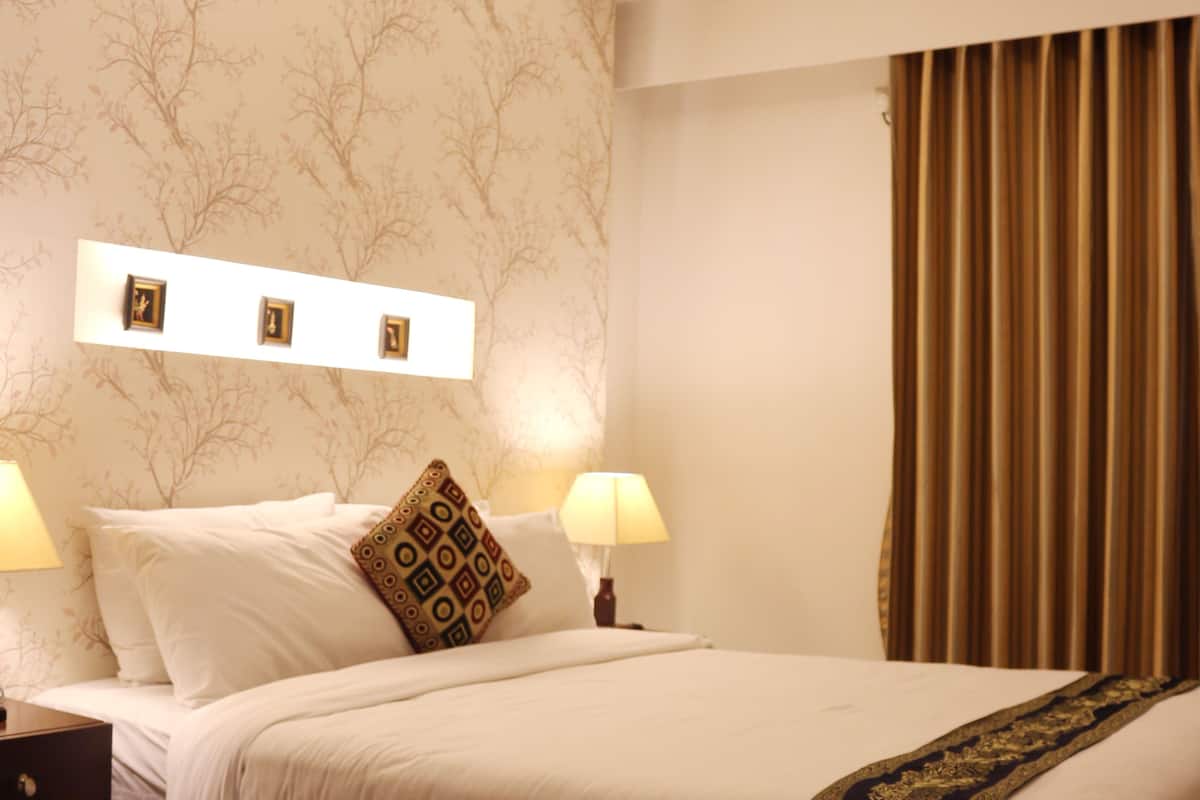 A hotel room with a bed, two bedside lamps, a wall-mounted air conditioner, and a curtain.