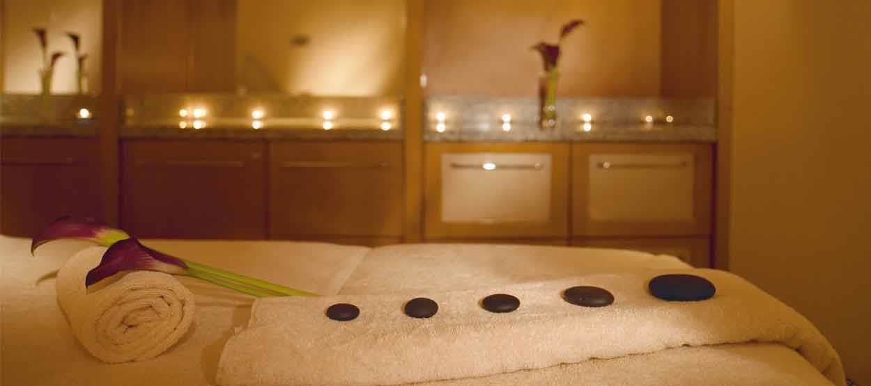 Une salle de spa avec une serviette, une serviette enroulée et une fleur sur un lit.