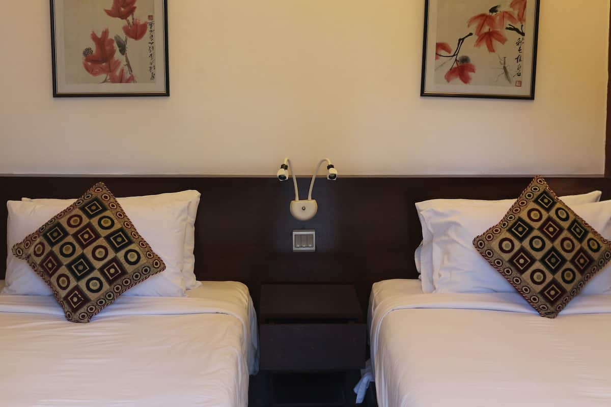 A hotel room with two beds, each with patterned pillows and framed floral artwork on the walls.