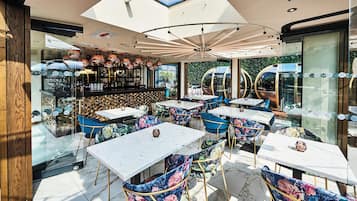 Un área de comedor al aire libre con mesas y sillas, una zona de bar con botellas y vistas a la vegetación.