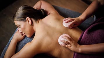 Eine Person erhält eine Rückenmassage mit zwei runden Massagegeräten auf einer dunklen Massageliege.