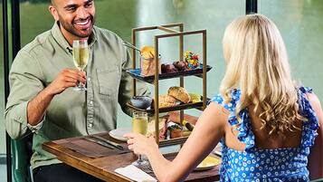 Un comedor con una mesa dispuesta para dos, un pastelero escalonado y vistas a un cuerpo de agua a través de una ventana.
