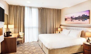 Habitación de hotel con una cama grande, un escritorio con lámpara, una silla y un televisor.