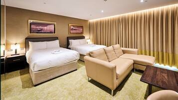 A hotel room with two beds, a sofa, a table, and curtains.