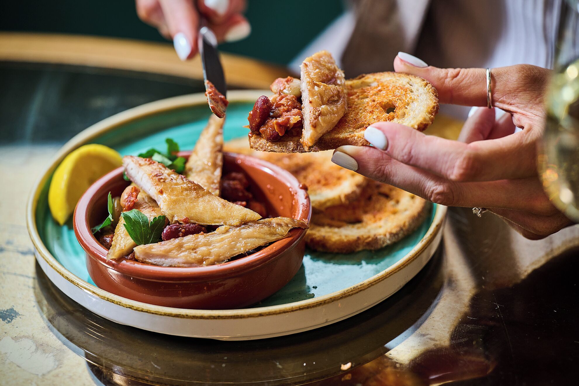 A person serving food from a terracotta bowl onto a slice of bread.