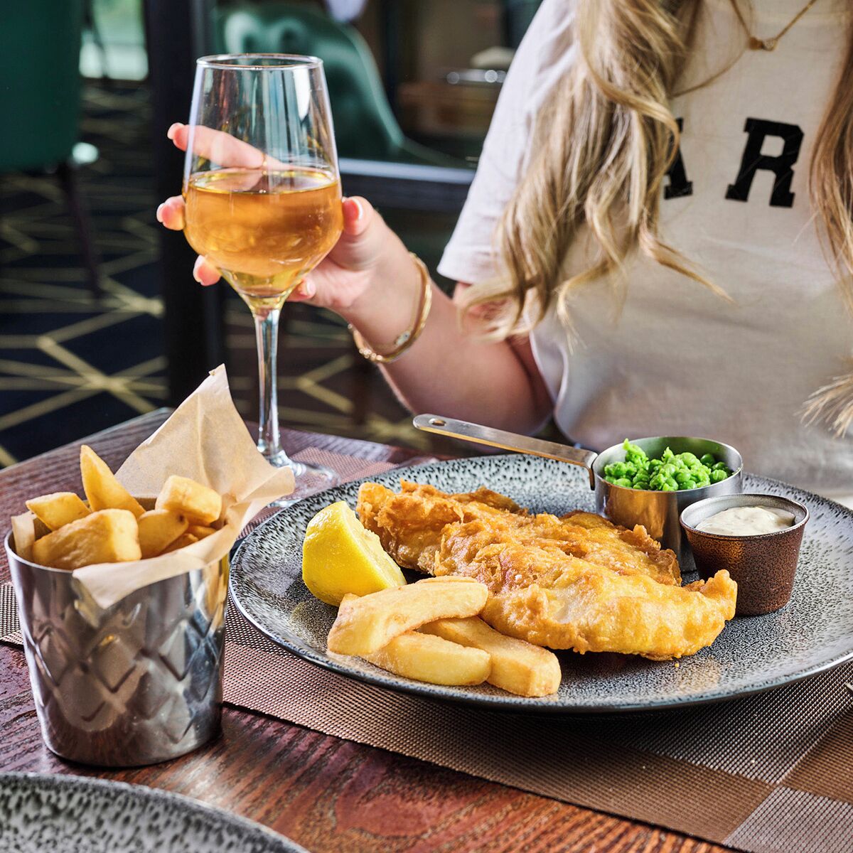 Ein Teller Fish and Chips mit einem Bierglas, einer kleinen Schale Erbsen und einer Tartarsauce.