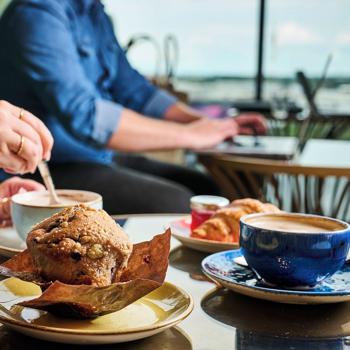 A table with a muffin, a cup of coffee, and a plate of food.
