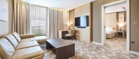 A hotel room with a sofa, a desk, a TV, and a bed.