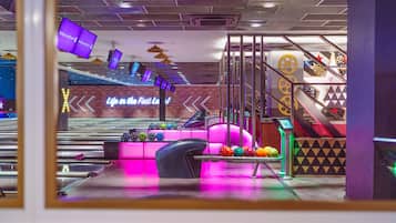 Un bowling avec un panneau au néon, une piste et des boules de couleurs vives.
