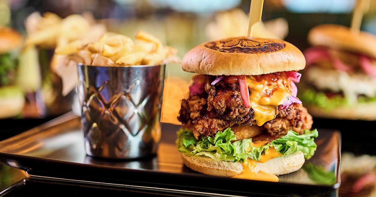 Un repas composé d'un hamburger servi dans un pain grillé, accompagné d'une portion de frites et d'une boisson servie dans un gobelet en métal.