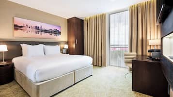 A hotel room with a large bed, a desk, a chair, a TV, and a window with curtains.