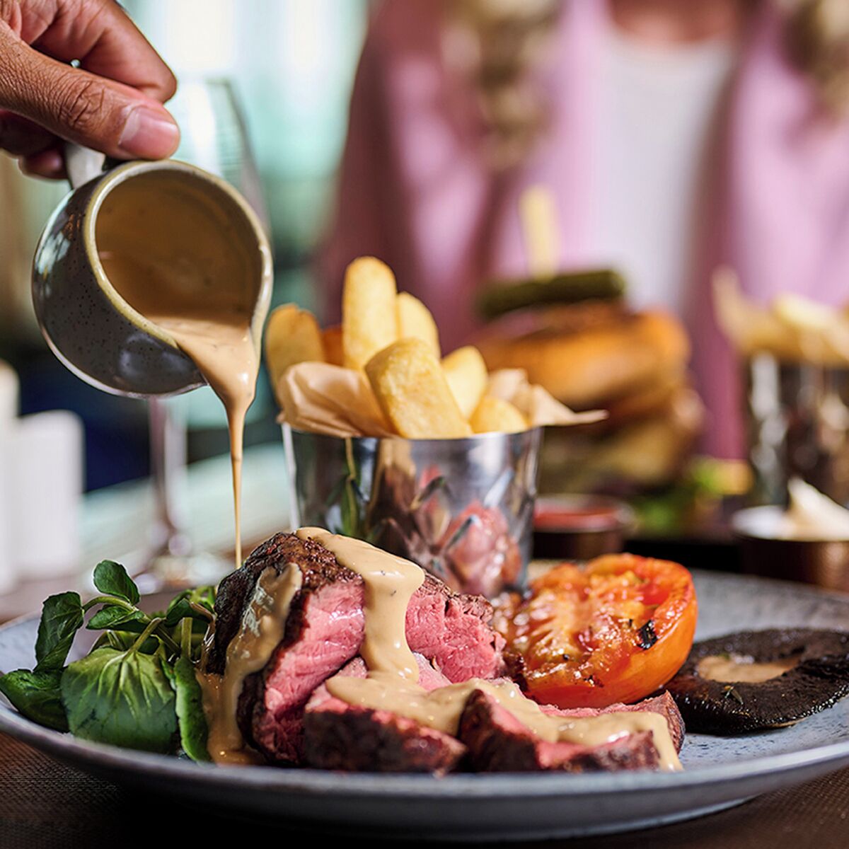 A plate of steak with sauce, fries, and a grilled tomato.