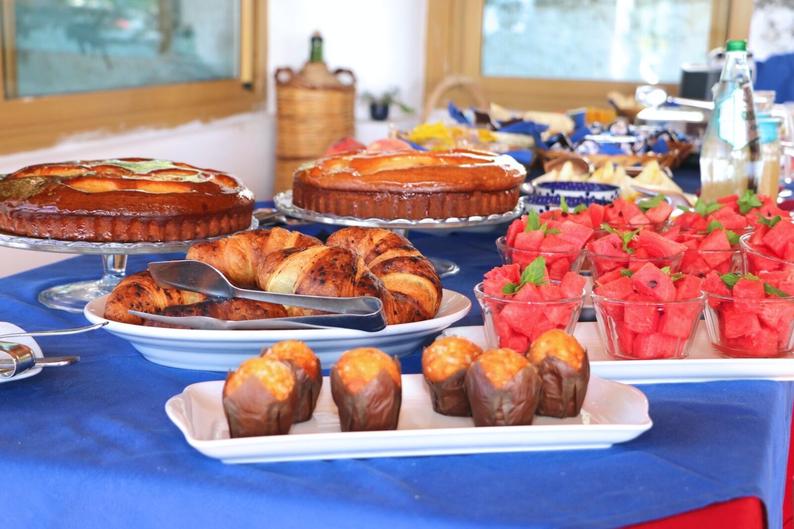 A buffet table with various food items including a pie, croissants, chocolate-covered treats, and watermelon cups.