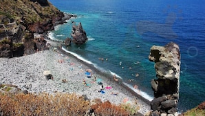 Una playa rocosa con aguas azul turquesa, gente nadando y tomando el sol.