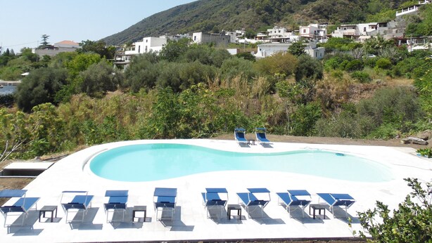 Una piscina con tumbonas y vistas a una ladera con edificios.