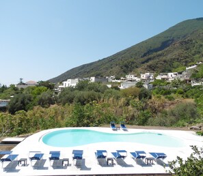 A swimming pool with sun loungers and a view of a hillside with buildings.