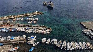 Un puerto deportivo con varias embarcaciones amarradas, un muelle y un gran barco al fondo.