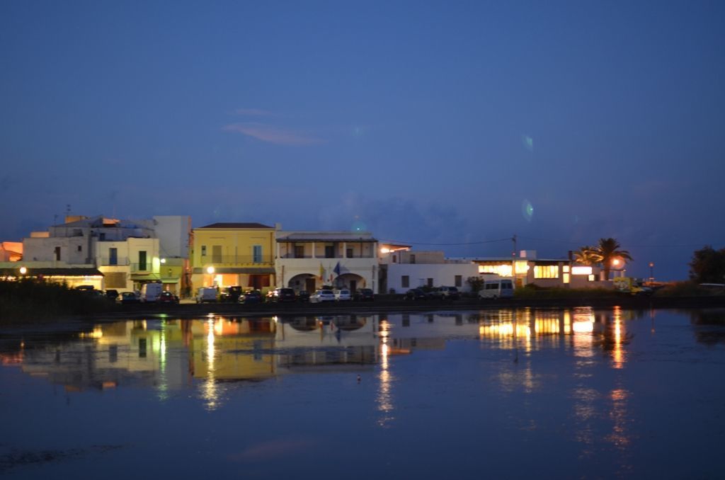 A waterfront property with buildings reflecting on calm water, featuring a mix of architectural styles and a serene evening ambiance.