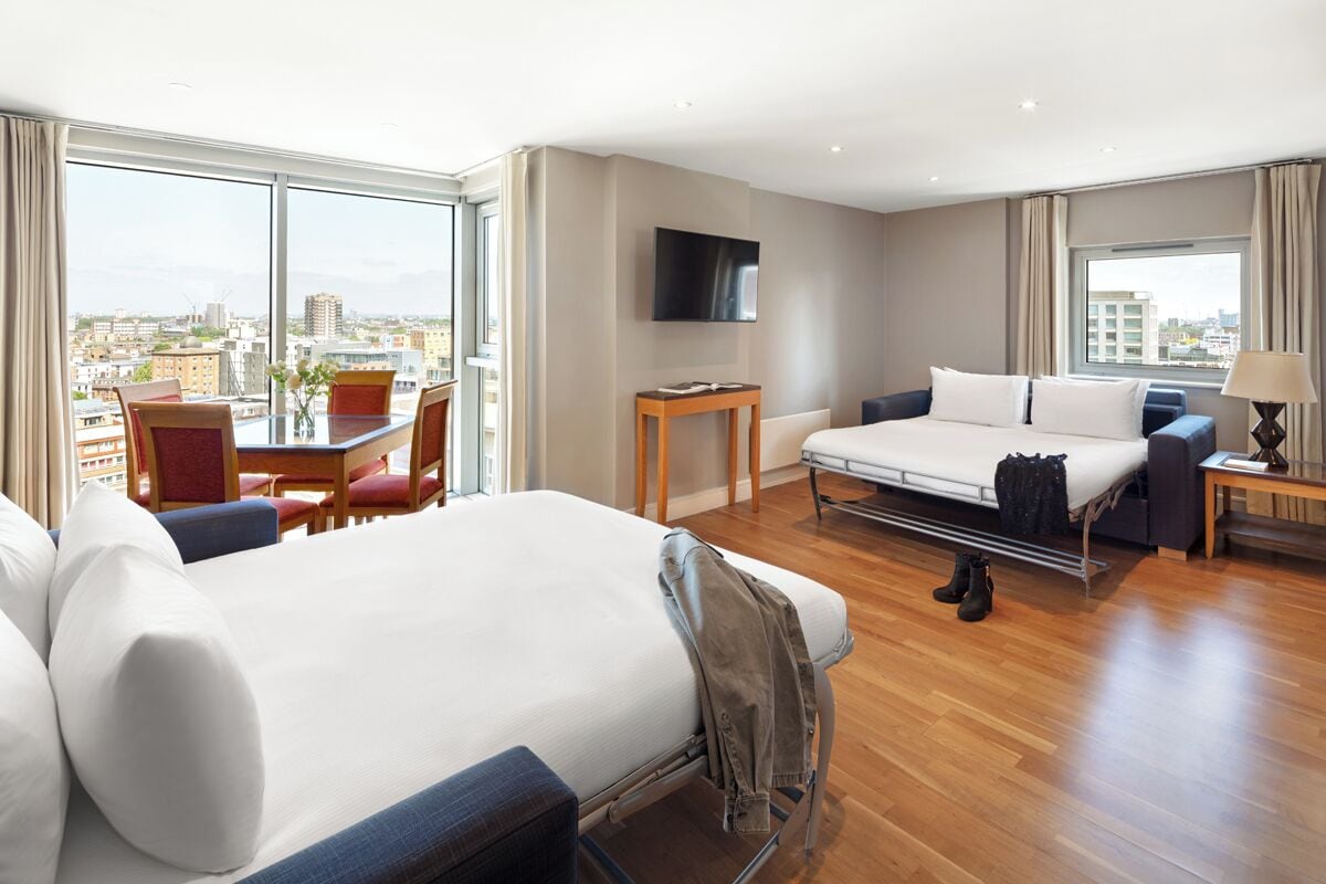 Habitación de hotel con cama, escritorio, silla, televisor y vista a la ciudad.