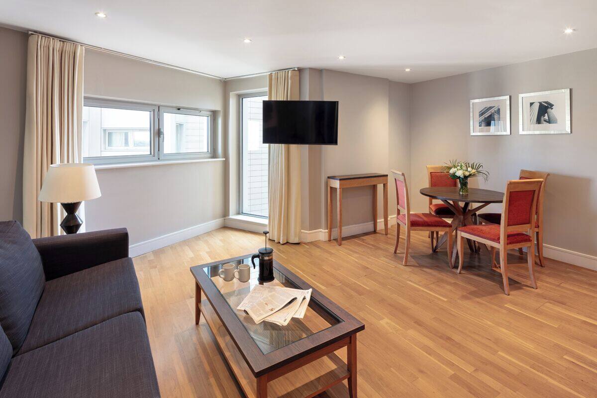 A modern living room with a sofa, a glass coffee table, a TV, and a dining area with chairs and a table.