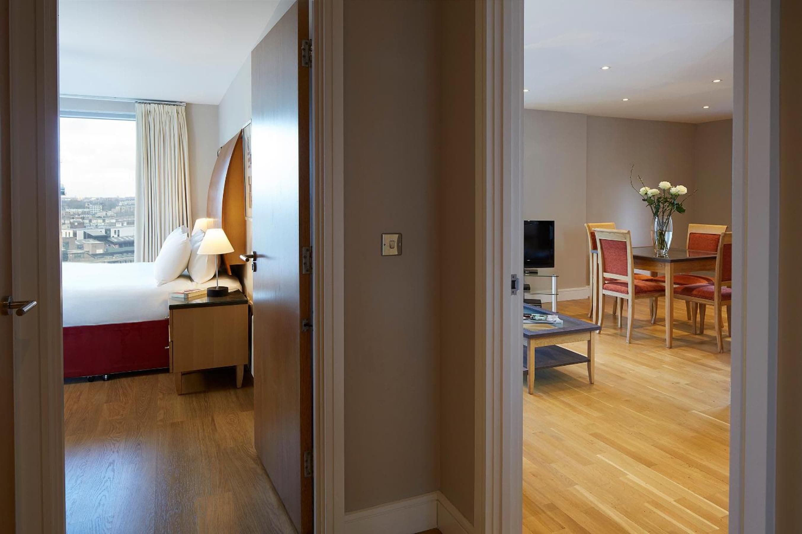 A hotel room with a bed, bedside table, lamp, and a view of the city.
