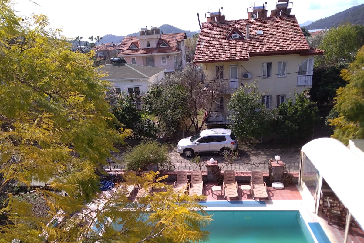 A residential area with a swimming pool, a parked car, and houses with red-tiled roofs.