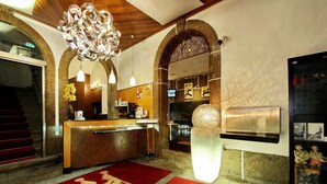 A hotel lobby with a reception desk, a large chandelier, and a red carpet with "M" and "A" letters. - Hotel Mestre de Avis (Guimarães)