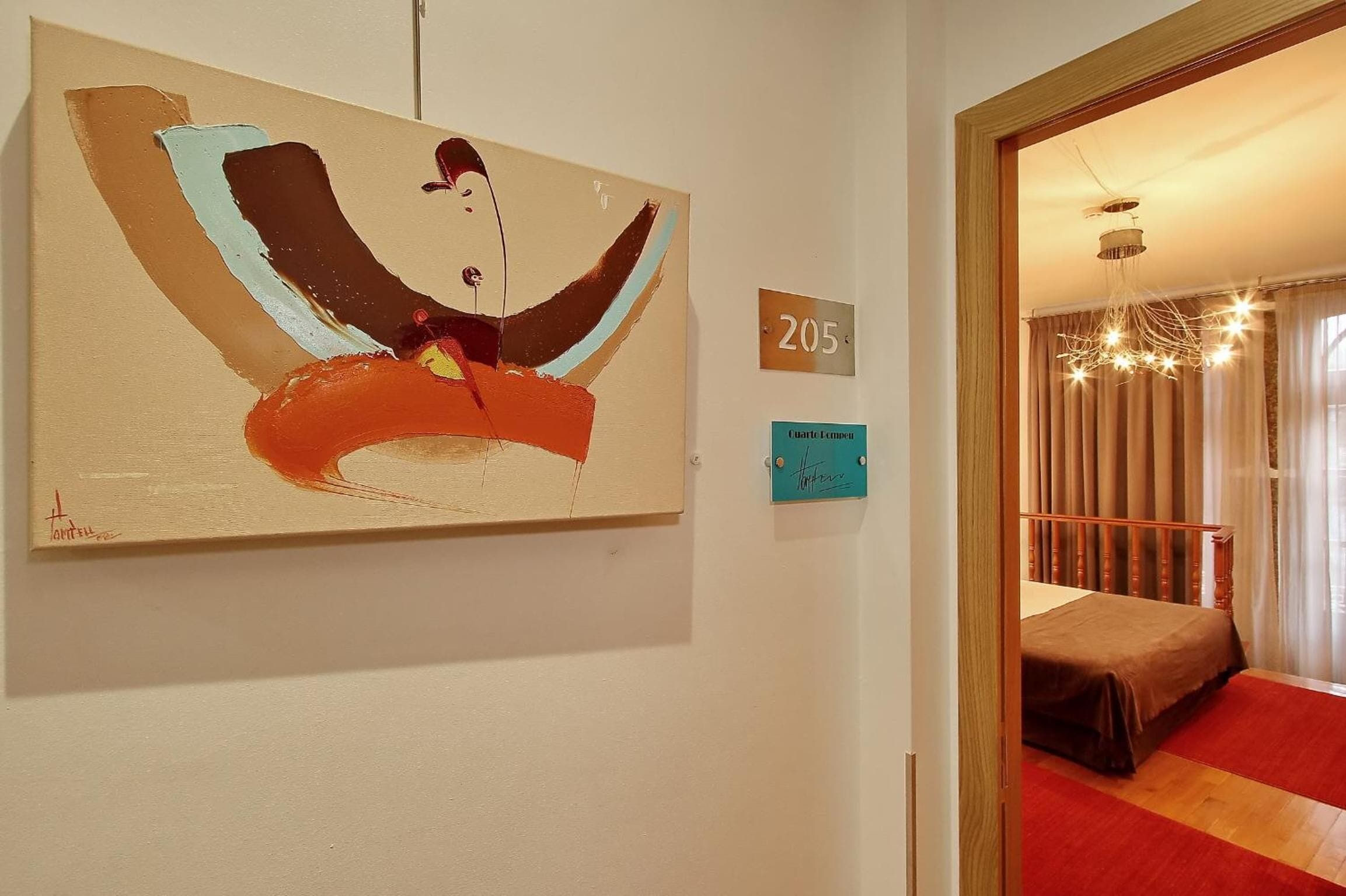 Een hotelkamer met een bed, een schilderij aan de muur en een bordje met het kamernummer 205.