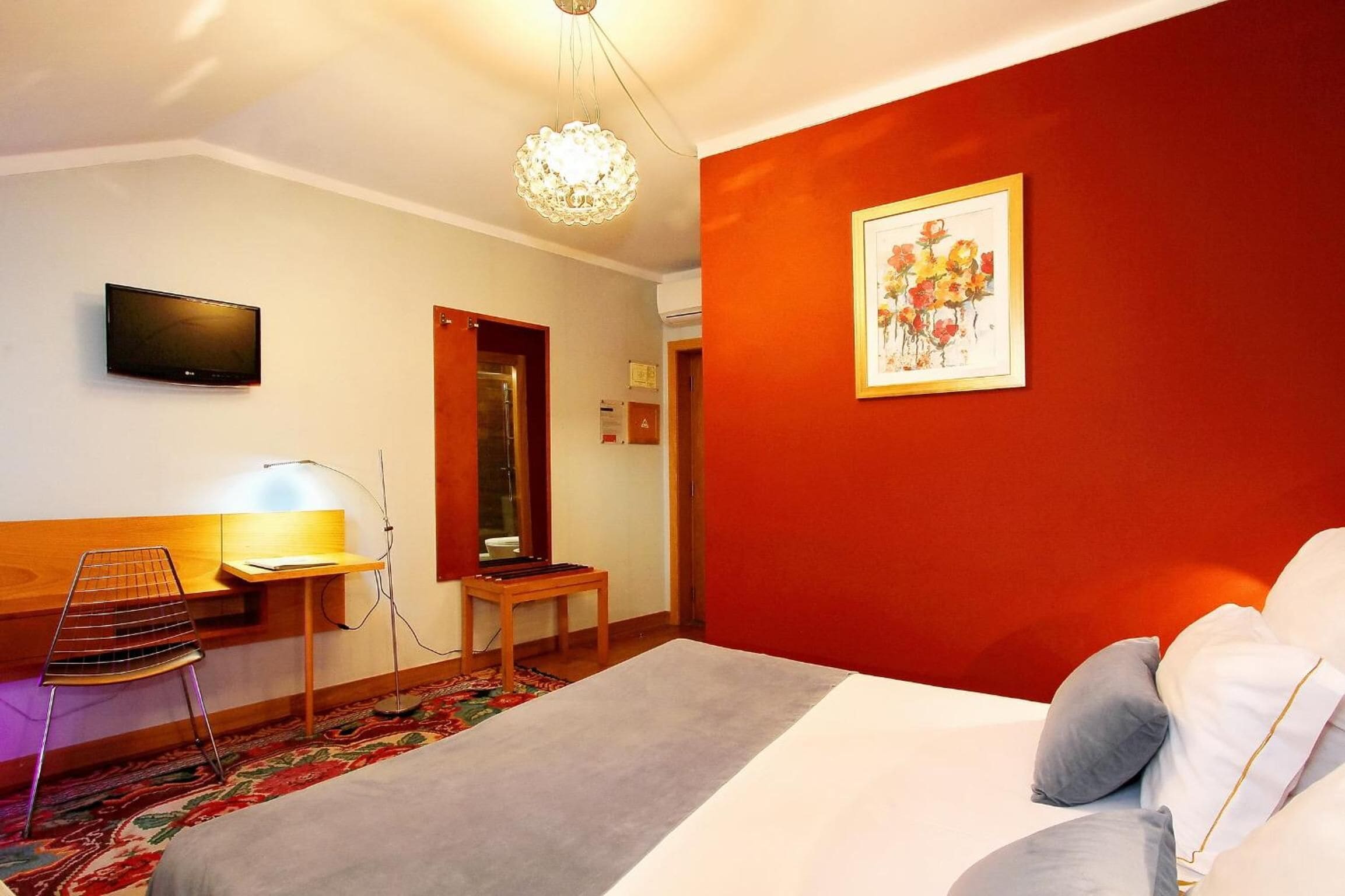 Una habitación de hotel con cama, escritorio, silla, televisor y un cuadro en la pared.