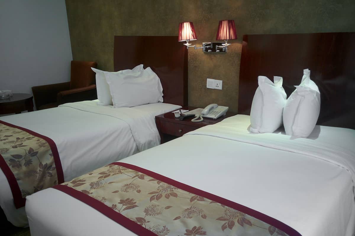 Ein Hotelzimmer mit zwei Betten, einem Nachttisch mit Telefon und einer Wandlampe.