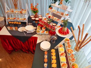 A buffet table with various food items and drinks, arranged on multiple tiers and accompanied by decorative elements like flowers and fruits.