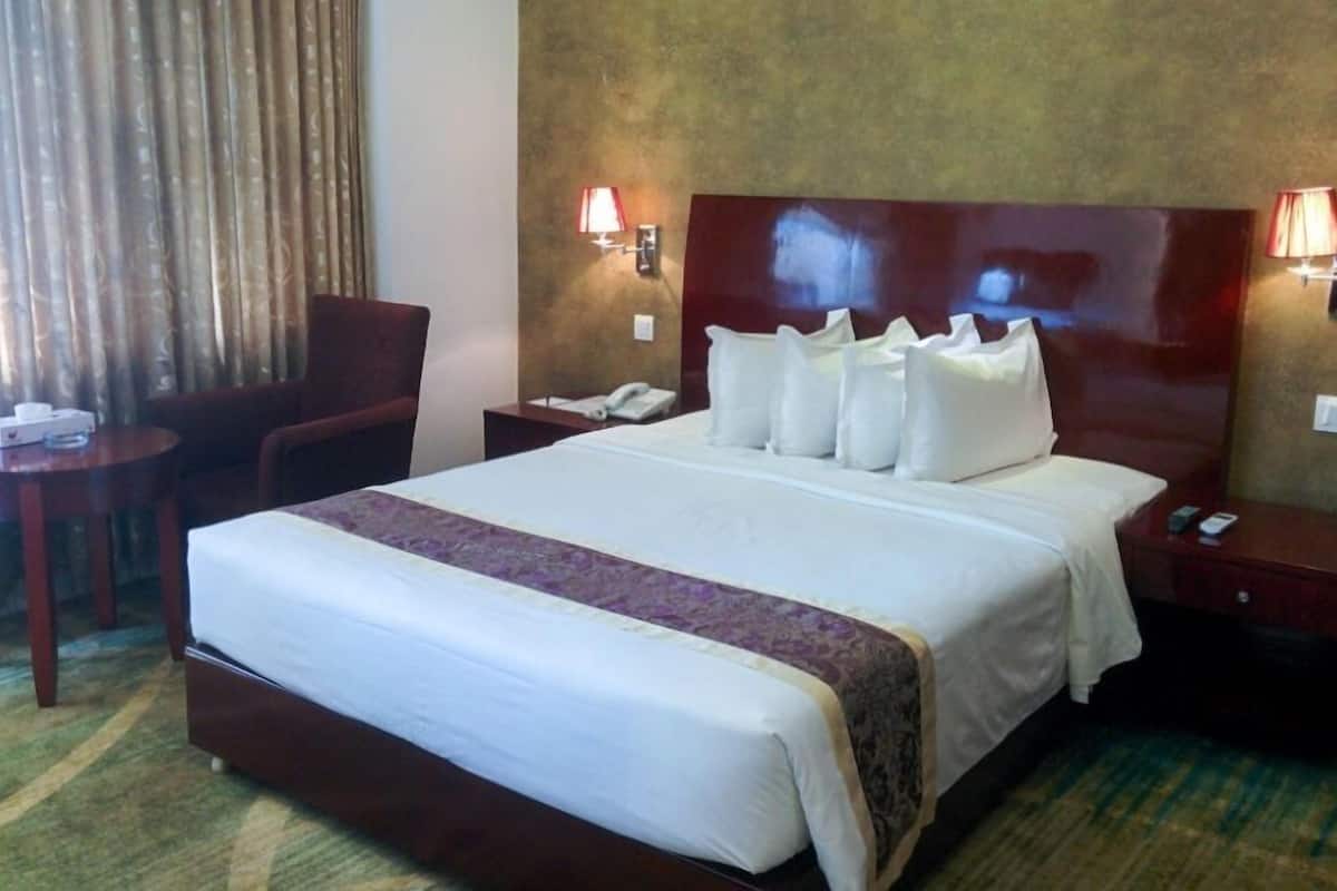 Ein Hotelzimmer mit einem großen Bett, einem Holz-Kopfstück, zwei Nachttischen, einem Sessel, einem Schreibtisch und einer Lampe.
