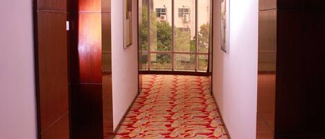 A narrow hallway with patterned carpet, wooden walls, and a large window at the end.